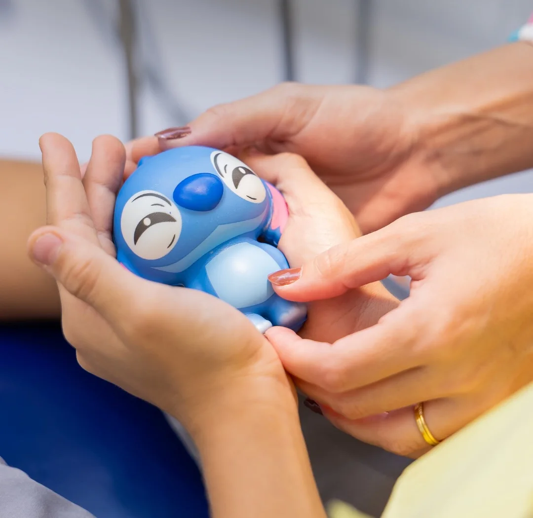As mãos da Dra. Letícia e as mãos de uma criança segurando juntas um bonequinho azul do Stitch