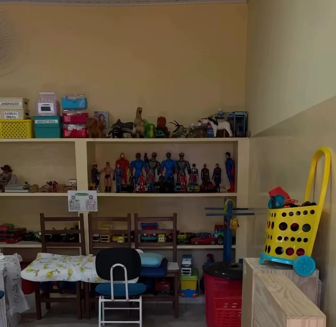 Brinquedoteca com prateleiras de bonecos e carrinhos, mesas e cadeiras infantis