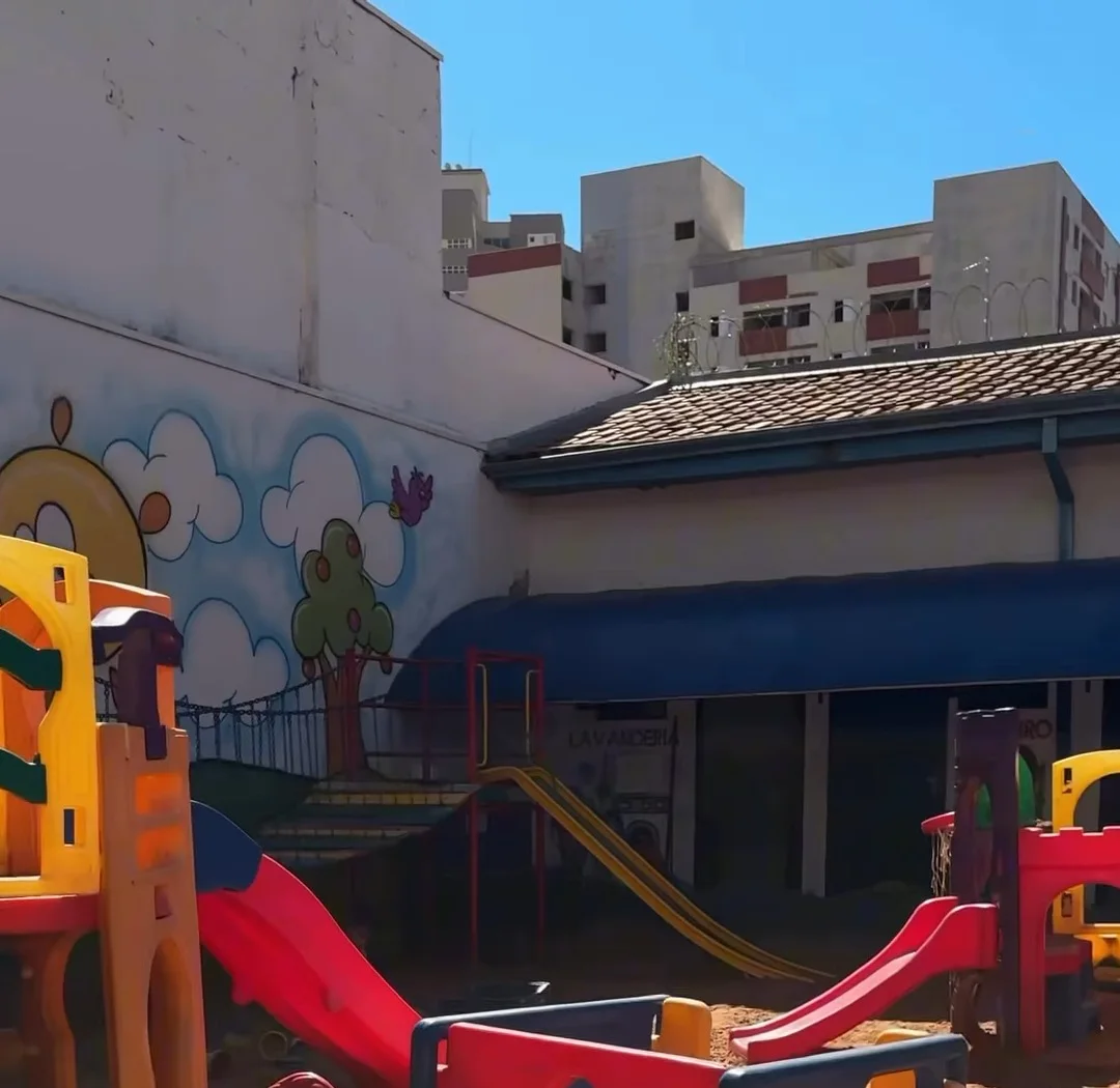 Parquinho de areia com escorregadores coloridos e muro pintado com nuvens