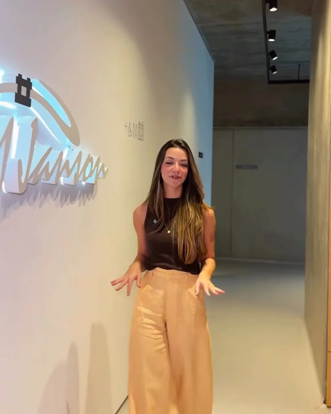 A Dra. Letícia caminhando no corredor, ao lado do letreiro iluminado MJanson na parede