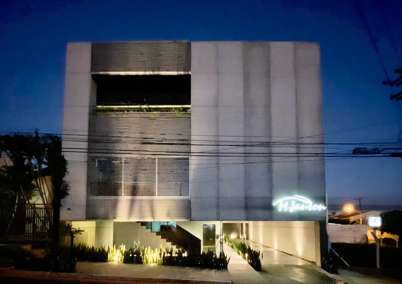 Fachada da Clínica MJanson à noite, com o letreiro iluminado e o jardim aceso