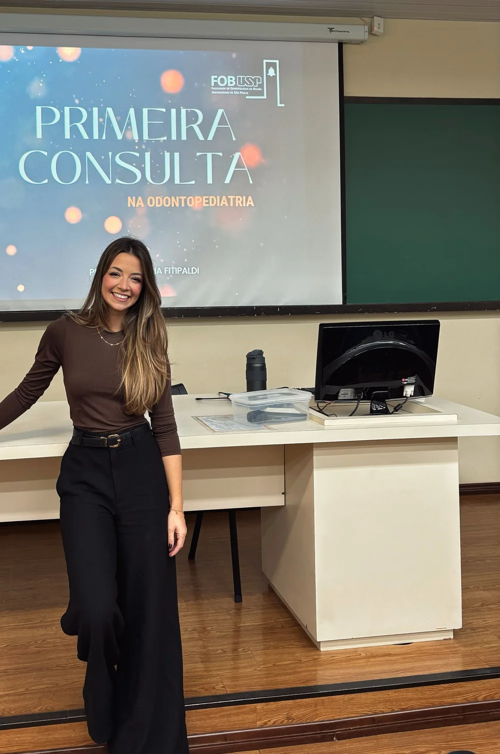 Letícia no auditório da FOB-USP, diante do slide “Primeira consulta na Odontopediatria”